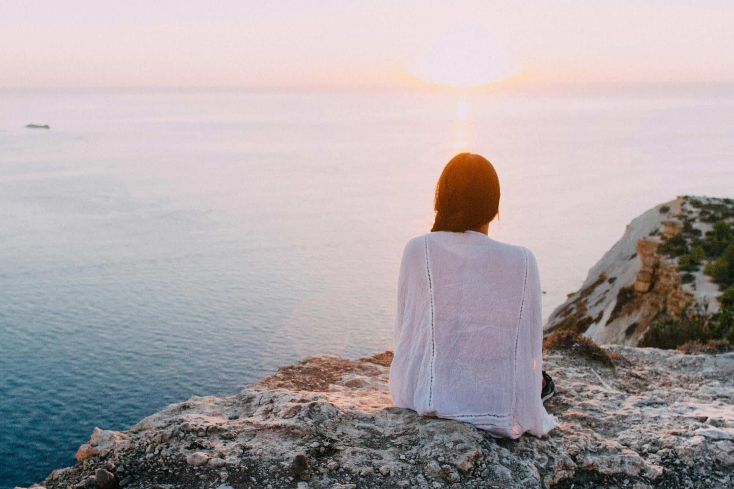 A Woman Sitting On A Rock Looking At The Sunset